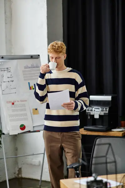A young professional sips coffee and reviews important documents in a stylish office setting. — Stock Photo