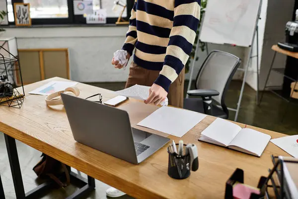 A young man in a striped sweater organizes documents at a sleek office desk during the day. — Stock Photo