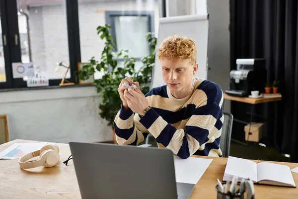 Young man in a striped sweater focuses on his tasks while seated at a sleek office desk. — Stock Photo