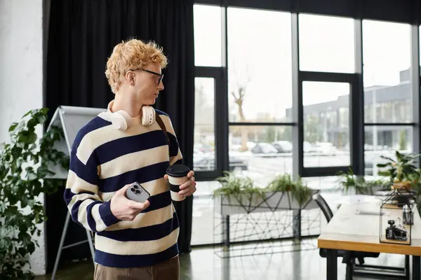 Uomo rosso in abbigliamento casual tiene un caffè e un telefono mentre si concentra sulle attività in un ufficio elegante. — Foto stock