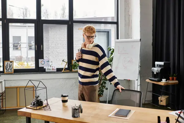 Um jovem ruivo em uma camisola listrada se prepara para o trabalho em um ambiente de escritório moderno. — Fotografia de Stock