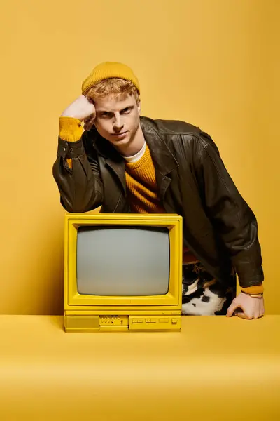 This stylish young man in a beanie poses confidently in a lively studio while leaning on a retro TV. — Stock Photo