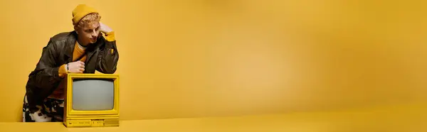 A stylish young man leaning on a retro TV on yellow background, banner — Stock Photo