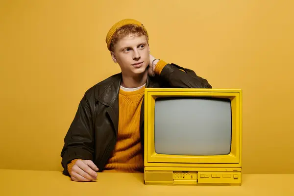 A fashionable young man poses confidently, dressed in warm winter attire leaning on a retro TV — Stock Photo