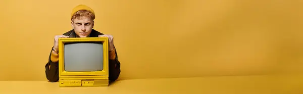 A stylish young redhead models trendy winter wear and leaning on a retro TV against a yellow background, banner — Stock Photo