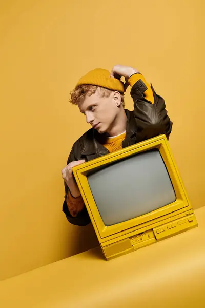 A fashionable young redhead models a winter outfit in a studio, standing with a retro television. — Stock Photo