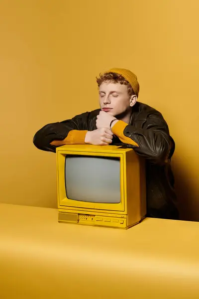 A fashionable young man with red hair relaxes beside a vintage yellow television in a studio. — Stock Photo