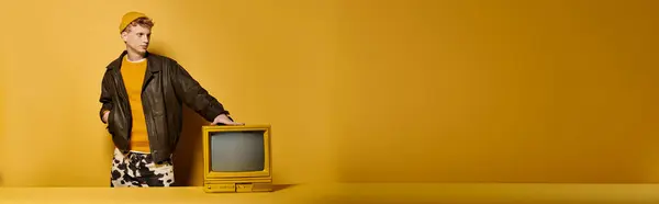 A stylish young man with red hair poses in a trendy winter outfit with a vintage television, banner — Stock Photo