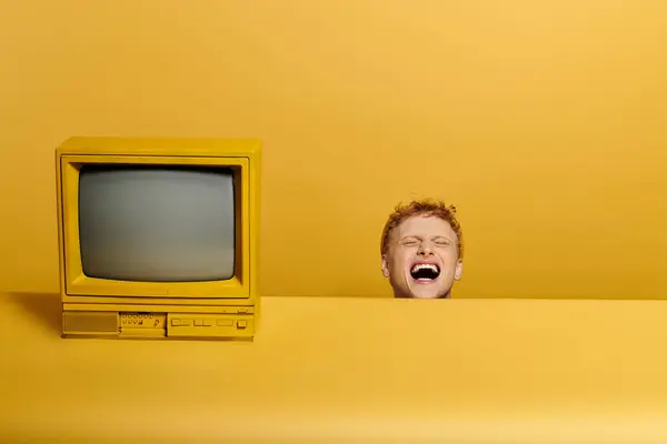 Elegante jovem ruiva exibe uma roupa de inverno na moda perto da televisão vintage em um estúdio amarelo animado. — Fotografia de Stock