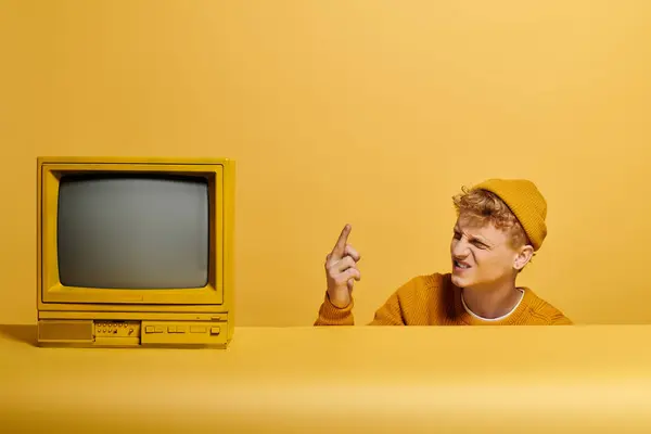 A young redhead in a stylish winter outfit near vintage television showcases his trendy style with a playful expression. — Stock Photo