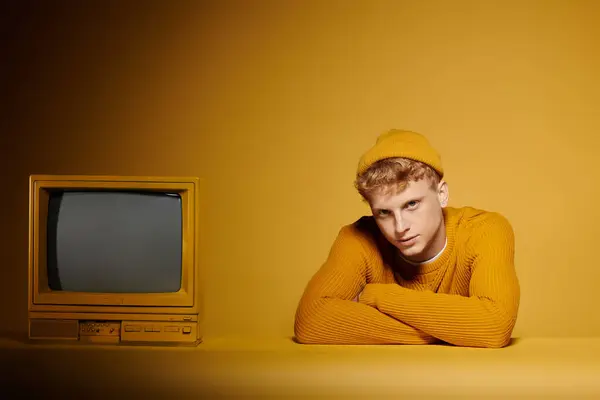 A stylish young redhead poses confidently in a cozy winter outfit near vintage television with a yellow background. — Stock Photo