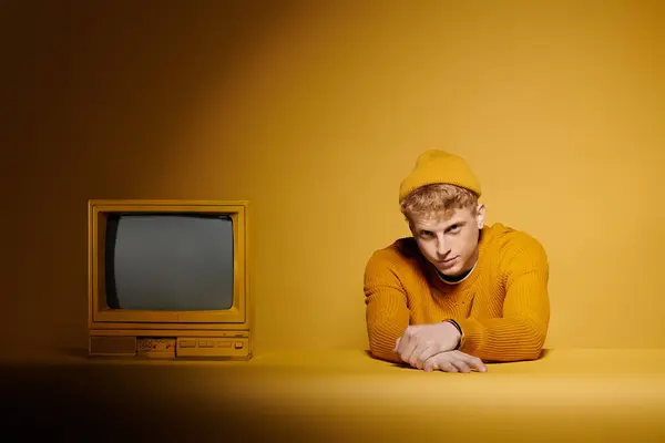 A young redhead shows off his stylish winter outfit near vintage television against a bright yellow background. — Stock Photo