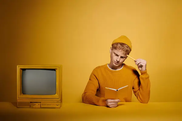 A fashionable young redhead man in a trendy winter outfit engages in reading while pondering near vintage television — Stock Photo
