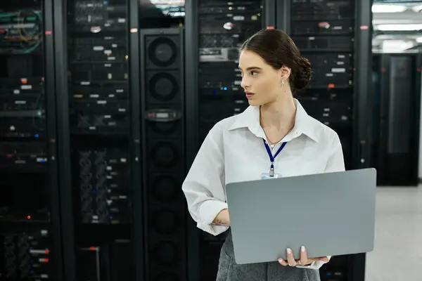 Donna in camicia bianca analizza i dati sul laptop in una moderna sala server focalizzata sull'efficienza. — Foto stock