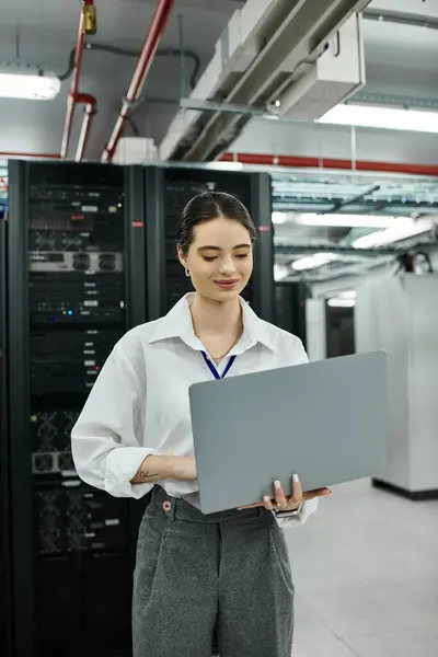 Una donna professionista in camicia bianca gestisce il suo computer portatile in un ambiente occupato sala server. — Foto stock