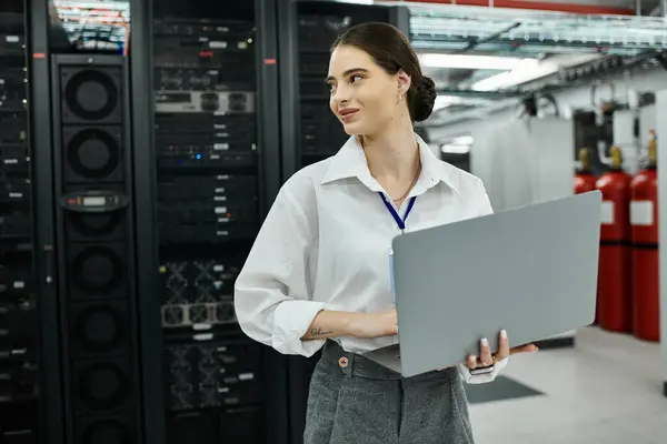 Eine selbstbewusste Frau im weißen Hemd sitzt mit ihrem Laptop in einem hochmodernen Serverraum. — Stockfoto