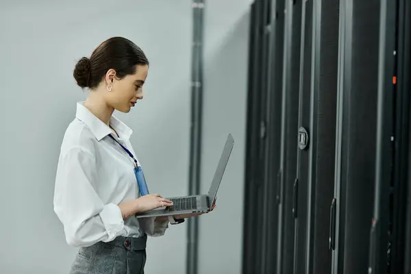 A professional in a white shirt works on a laptop in a modern server room. — Stock Photo