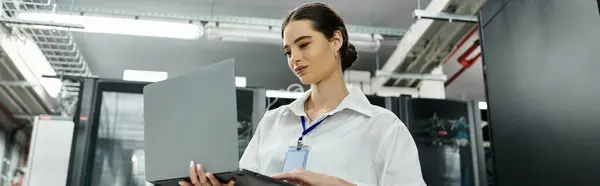 A focused IT specialist in a white shirt works on a laptop in a data center, banner — Stock Photo