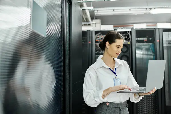 Una donna dedicata in camicia bianca lavora diligentemente su un computer portatile in un ambiente elegante sala server. — Foto stock