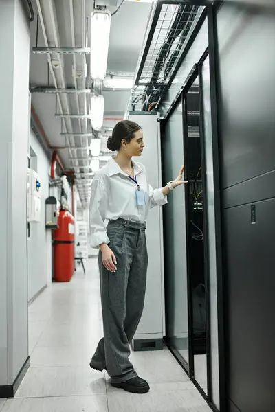 Una donna con una camicia bianca ispeziona l'hardware del server garantendo al contempo la sicurezza digitale in un ambiente tecnologico. — Foto stock