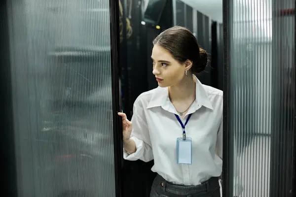 Mujer con camisa blanca navega por una sala de servidores mientras monitorea los sistemas informáticos. - foto de stock