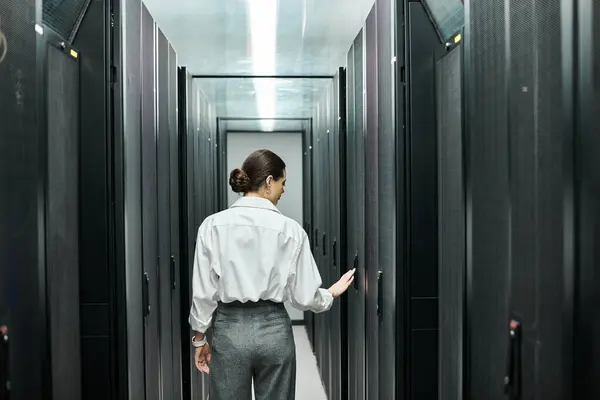 Professional woman in a white shirt works diligently among server racks in a data center. — Stock Photo