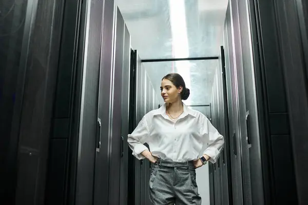 Eine kompetente Frau in weißem Hemd steht selbstbewusst zwischen Serverschränken in einem Rechenzentrum. — Stockfoto