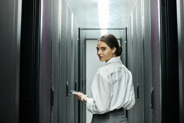 Frau im weißen Hemd arbeitet aufmerksam in einem schlanken Serverraum und sorgt für Systemfunktionalität. — Stockfoto