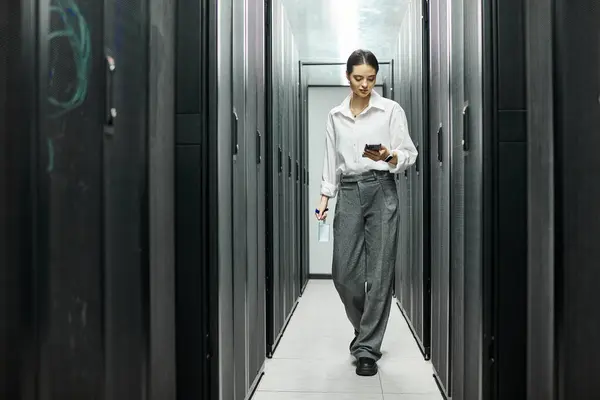 Una donna in camicia bianca naviga attraverso una sala server, impegnandosi con la tecnologia. — Foto stock