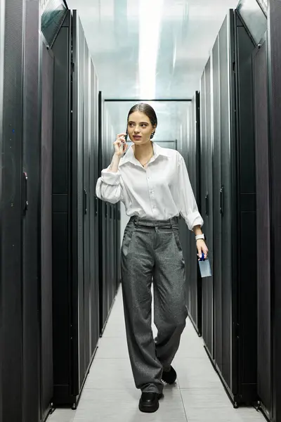 Una donna in camicia bianca lavora sodo in una moderna sala server, mantenendo i sistemi funzionanti senza intoppi. — Foto stock
