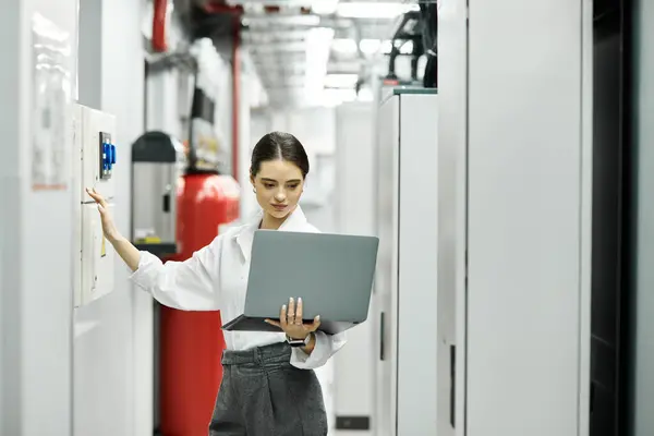 Una donna con una camicia bianca si concentra sul suo computer portatile mentre controlla i sistemi in una stanza del server. — Foto stock