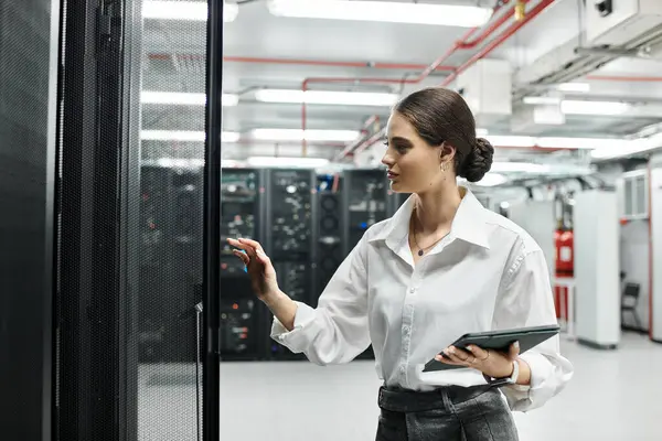 Una donna esperta in camicia bianca lavora in una moderna sala server, supervisionando i sistemi. — Foto stock