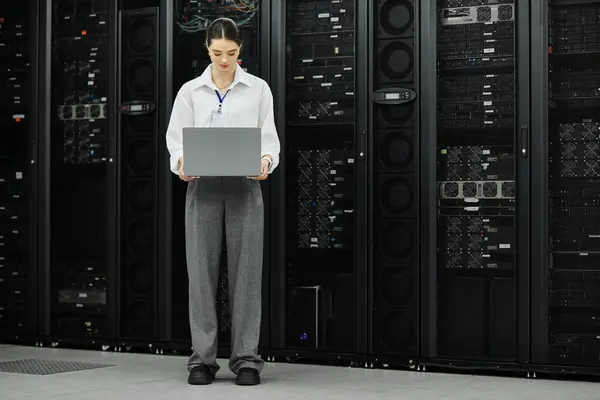 Una donna con una camicia bianca lavora con un computer portatile, assicurando operazioni fluide in una sala server. — Foto stock