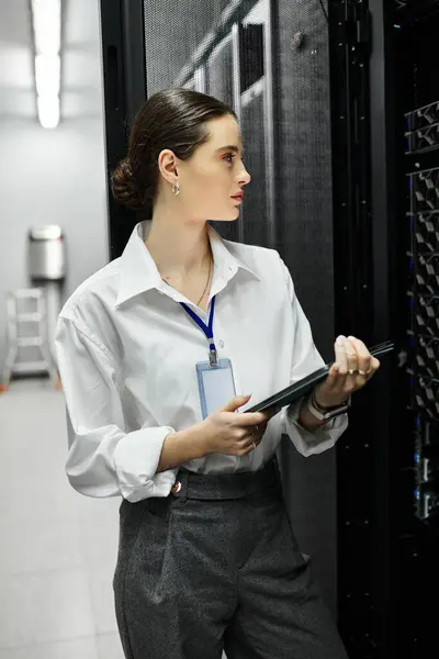 Donna focalizzata in camicia bianca lavora in una sala server ad alta tecnologia, gestendo le operazioni di rete. — Foto stock