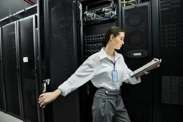 Eine Frau im weißen Hemd arbeitet intensiv in einem modernen Serverraum und richtet Netzwerkkonfigurationen ein. — Stockfoto