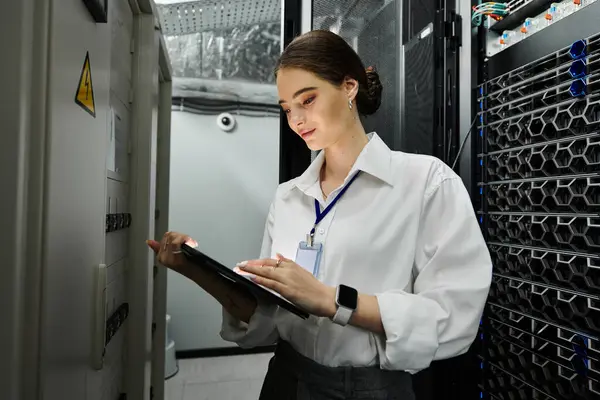 Donna in camicia bianca monitora diligentemente i sistemi server in un data center high-tech. — Foto stock