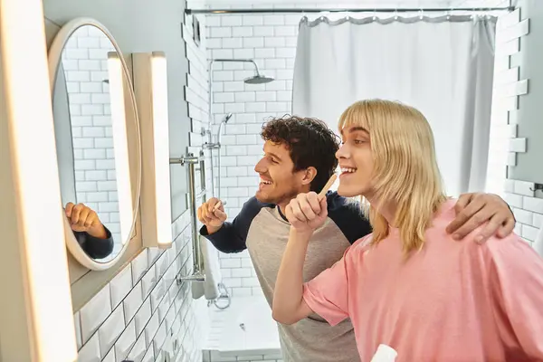 Two men happily brush their teeth together in a cozy, modern bathroom filled with natural light. — Stock Photo
