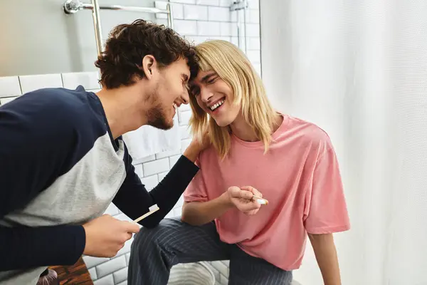 Two loving men smile at each other while enjoying their morning routine in a bright bathroom. — Stock Photo