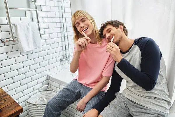 Two happy men brush their teeth together, sharing laughter and love in a bright bathroom. — Stock Photo