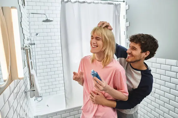 Two men enjoy a playful moment as one styles the others hair with laughter in a stylish bathroom. — Stock Photo