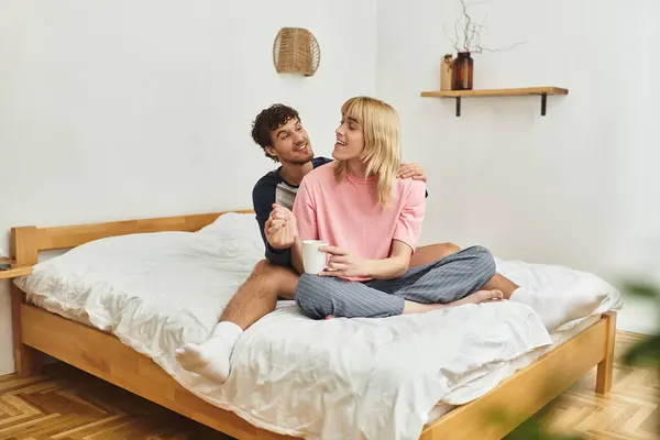 Two men enjoy a serene morning on a comfortable bed, sharing laughter and a warm drink together. — Stock Photo