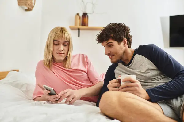 A loving gay couple enjoys quality time together while relaxing in bed and browsing on a smartphone. — Stock Photo