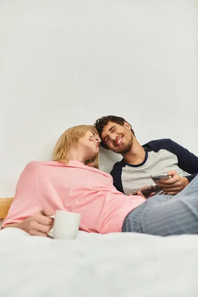 Two men share laughter and affection while cuddling on a soft bed with coffee cups nearby. — Stock Photo