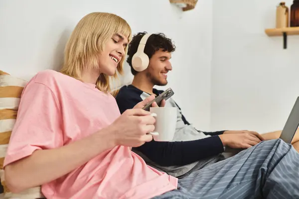 Dos hombres disfrutan de la compañía de los demás en casa, interactuando con sus dispositivos mientras beben. - foto de stock