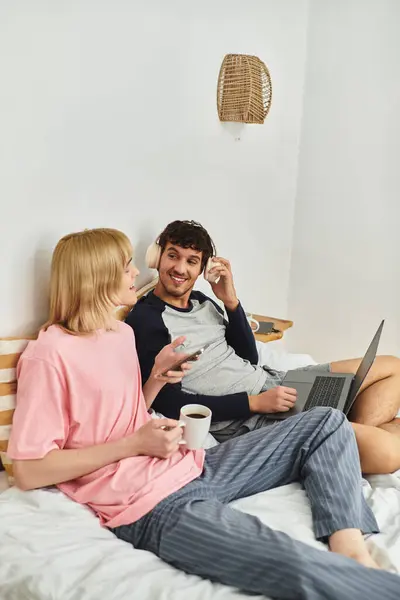Couple relaxes in their stylish bedroom, sharing a warm moment while sipping coffee and chatting. — Stock Photo