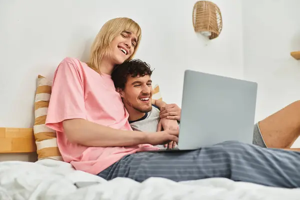 Two men cuddle closely together on a bed, enjoying each others company as they share fun online. — Stock Photo