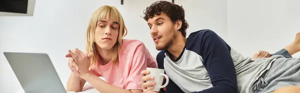 Deux hommes se détendent dans leur chambre, engagés dans la conversation tout en utilisant un ordinateur portable et en sirotant des boissons. — Photo de stock