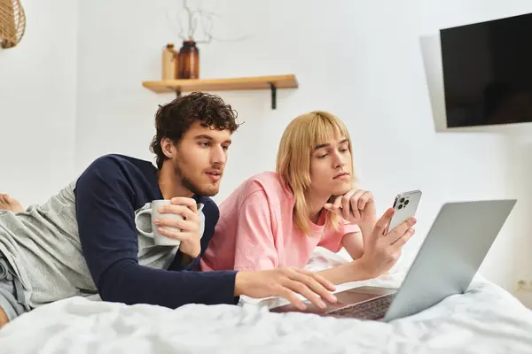 Two men relax on their bed, sharing laughs as they explore their devices in a cozy setting. — Stock Photo