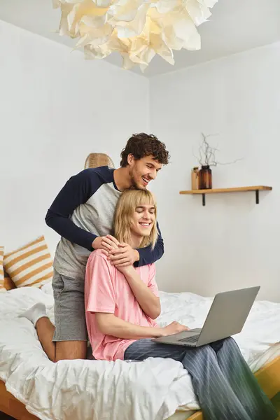 A loving gay couple shares laughter and warmth while working on a laptop in their cozy bedroom. — Stock Photo