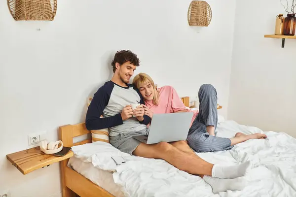 Two men joyfully share a moment together while working on a laptop in their cozy bedroom. — Stock Photo